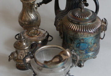 Ensemble en métal argenté comprenant une petite cafetière, une boîte couverte, une théière, un sucrier le récipient en verre gravé (manque le couvercle), une petite fontaine et un sucrier couvert uniplat.