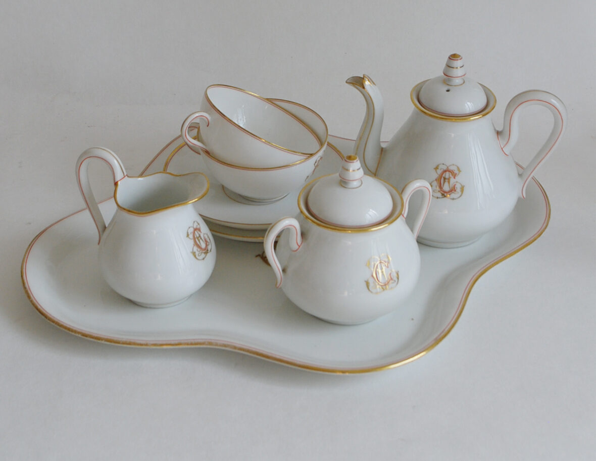 Service à thé en porcelaine à filets rouge et or, monogrammé HC et comprenant une théière, un sucrier, un pot à lait, deux tasses et soucoupes et un plateau de forme quadrilobée.