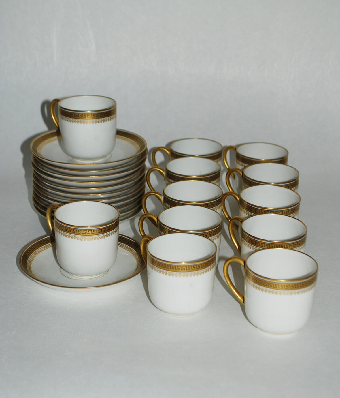 Partie de service à café en porcelaine à décor doré de frise de grecques et palmettes comprenant 12 tasses et sous tasses. Signé D&C France.