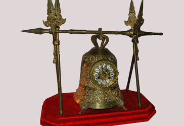 Pendule en bronze doré représentant une cloche tenue par des lances, le cadran à médaillon émaillé blanc et chiffres romains. Socle en velours rouge. De style gothique.
