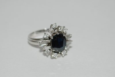 Bague en or gris de forme marguerite ornée d’un saphir central et entourée de diamants brillants et baguettes.